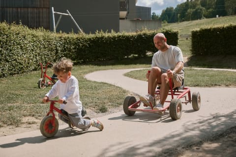Kleinkind auf dem Laufrad, Papa im Tretauto auf dem Rundkurs